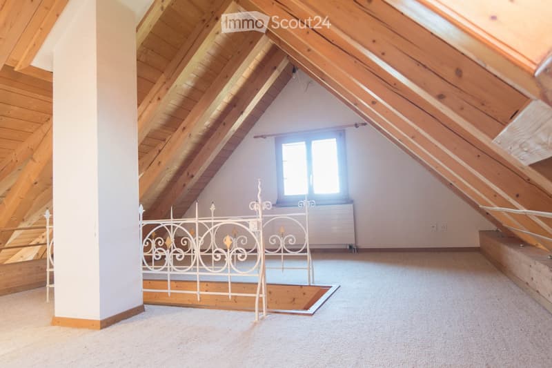 An attic space with wooden beams, a window, and a decorative white metal railing, but no furniture or furnishings.