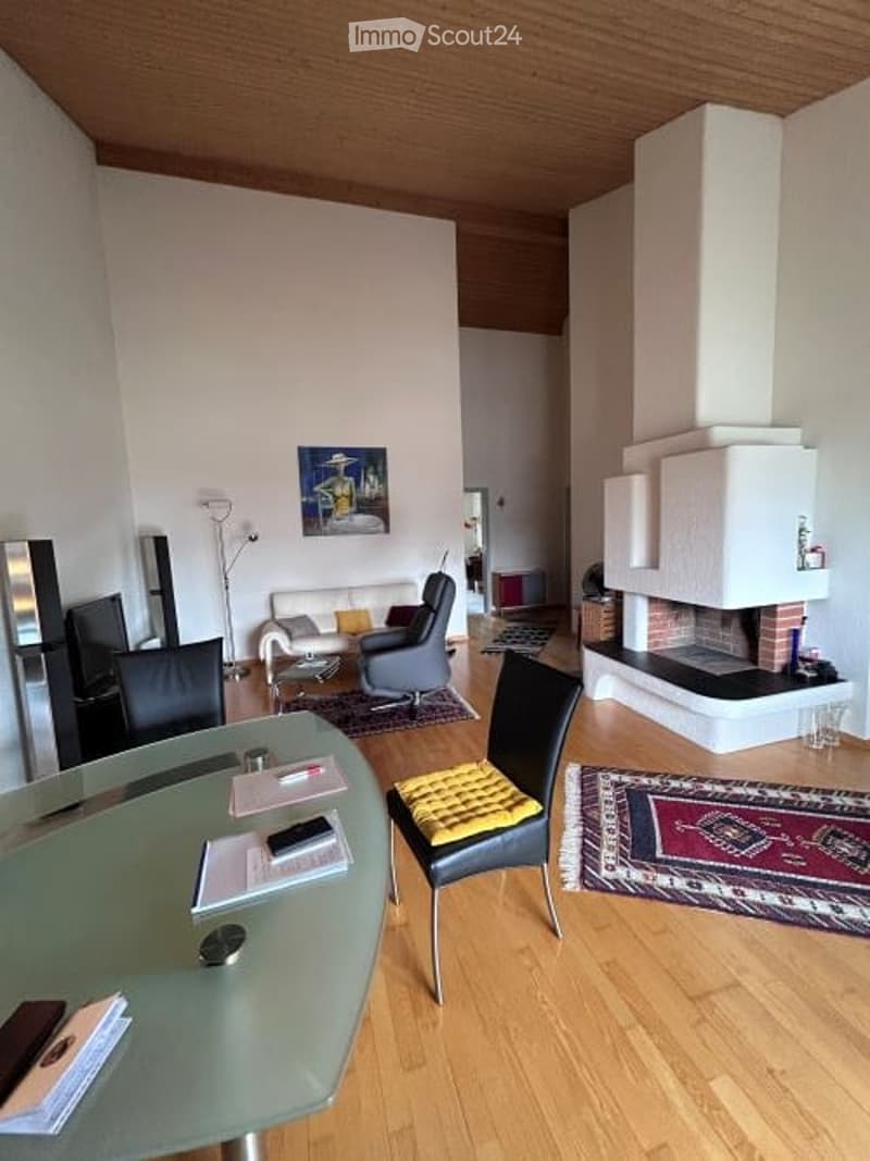 Modern living room with a fireplace, white sofa, grey armchair, glass coffee table, and a colorful rug on the wooden floor.