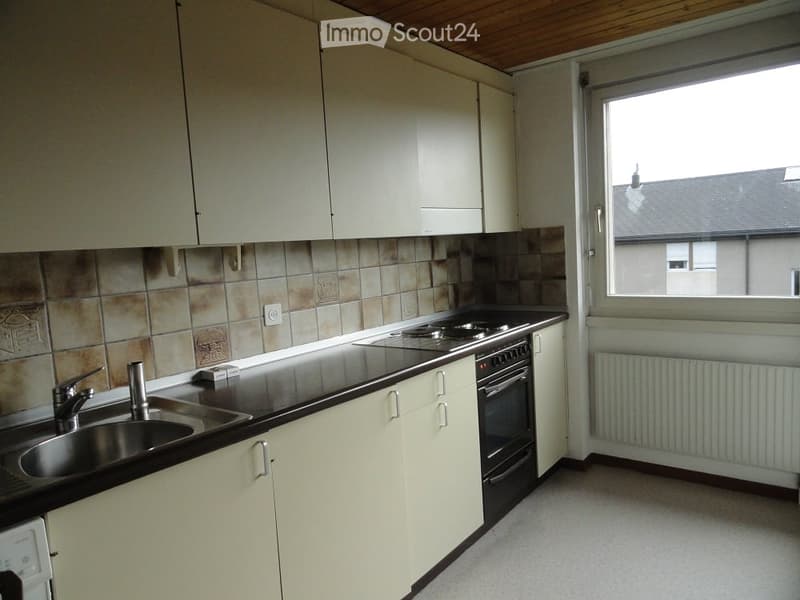 Modern kitchen with white cabinets, black countertop, stainless steel sink, and built-in oven. Features a window with a view of a building outside.