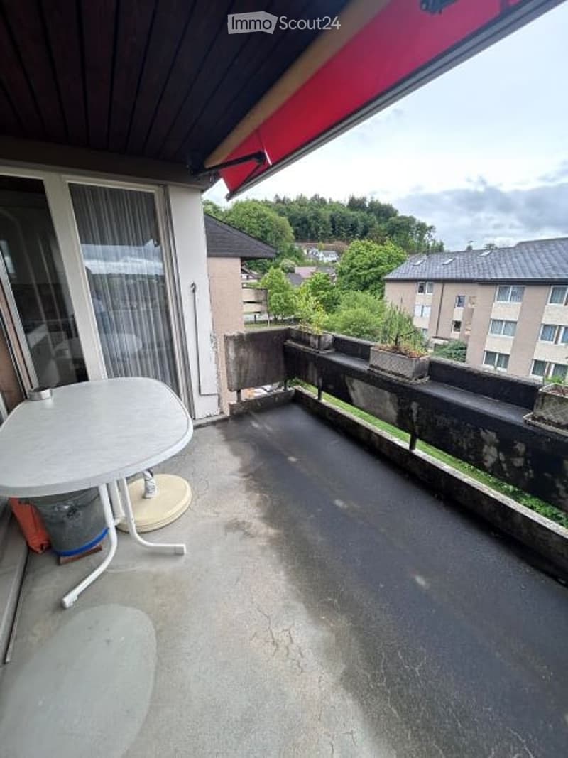 Balcony with a small table, chairs, and a view of the surrounding area with buildings and greenery.