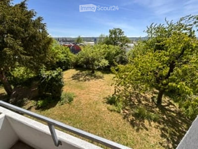 Balcony overlooking a green garden area with trees and a distant view of buildings.