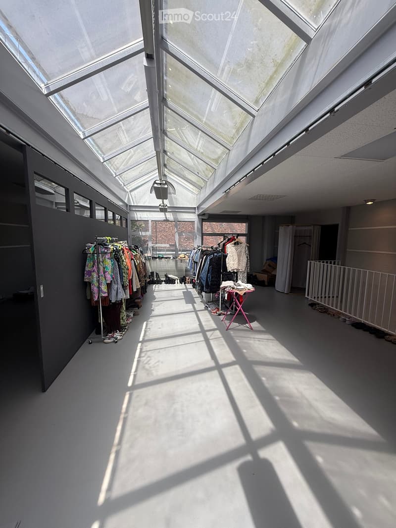 Bright, open space with a high ceiling and skylights, featuring clothing racks, a small table, and a curtained area.