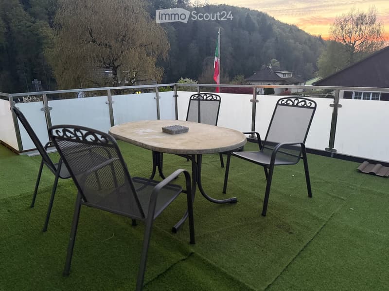 Balcony with artificial grass, round table, four chairs, and a flag in the background.
