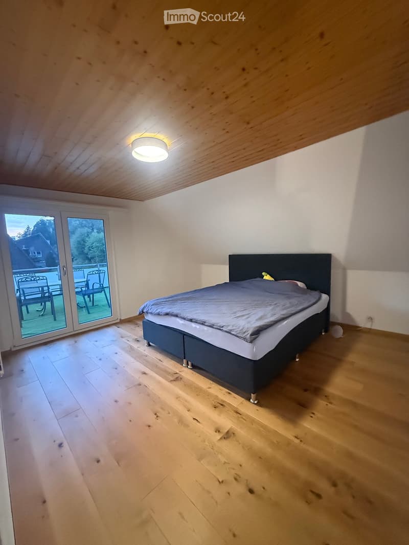 Bedroom with wooden floor, bed with headboard, large window with balcony access, and modern lighting fixture.