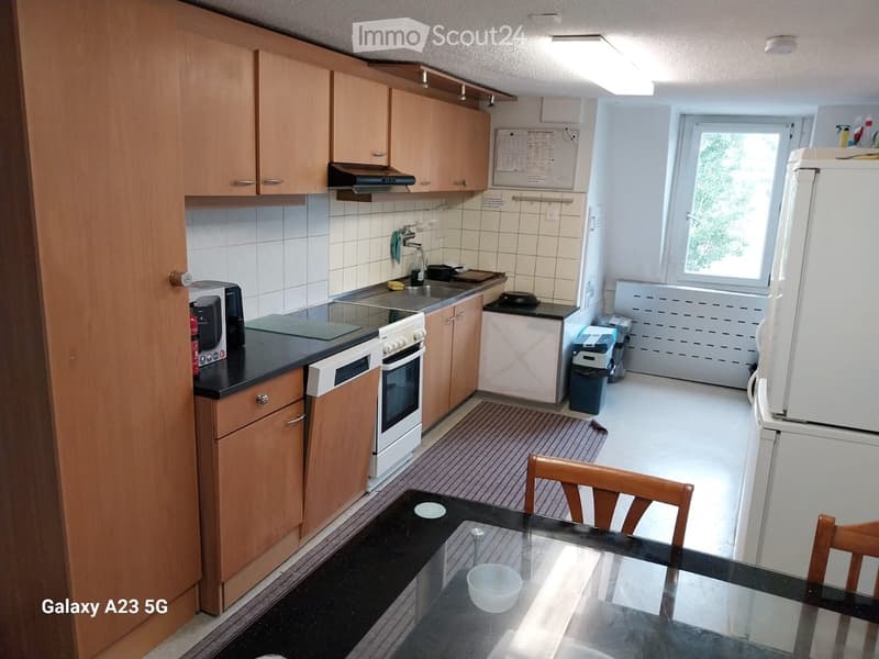 A well-lit kitchen with wooden cabinets, a black countertop, a white oven, a microwave, a sink, a refrigerator, and a dining area with a glass table and wooden chairs.