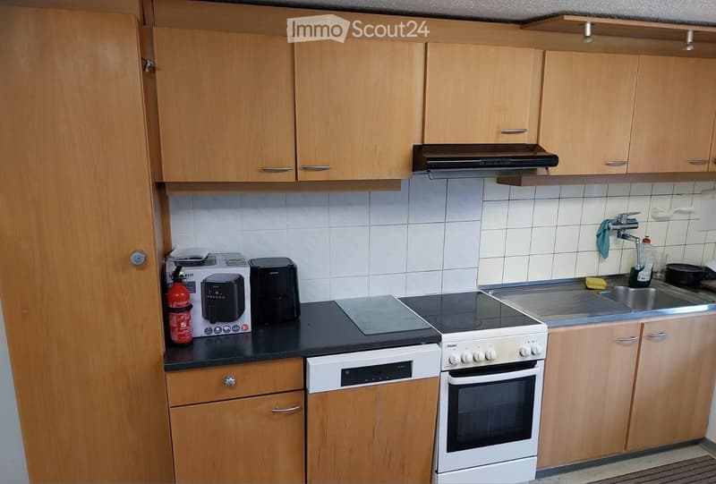 Modern kitchen with wooden cabinets, white tiles, and stainless steel appliances including an oven, fridge, and sink.