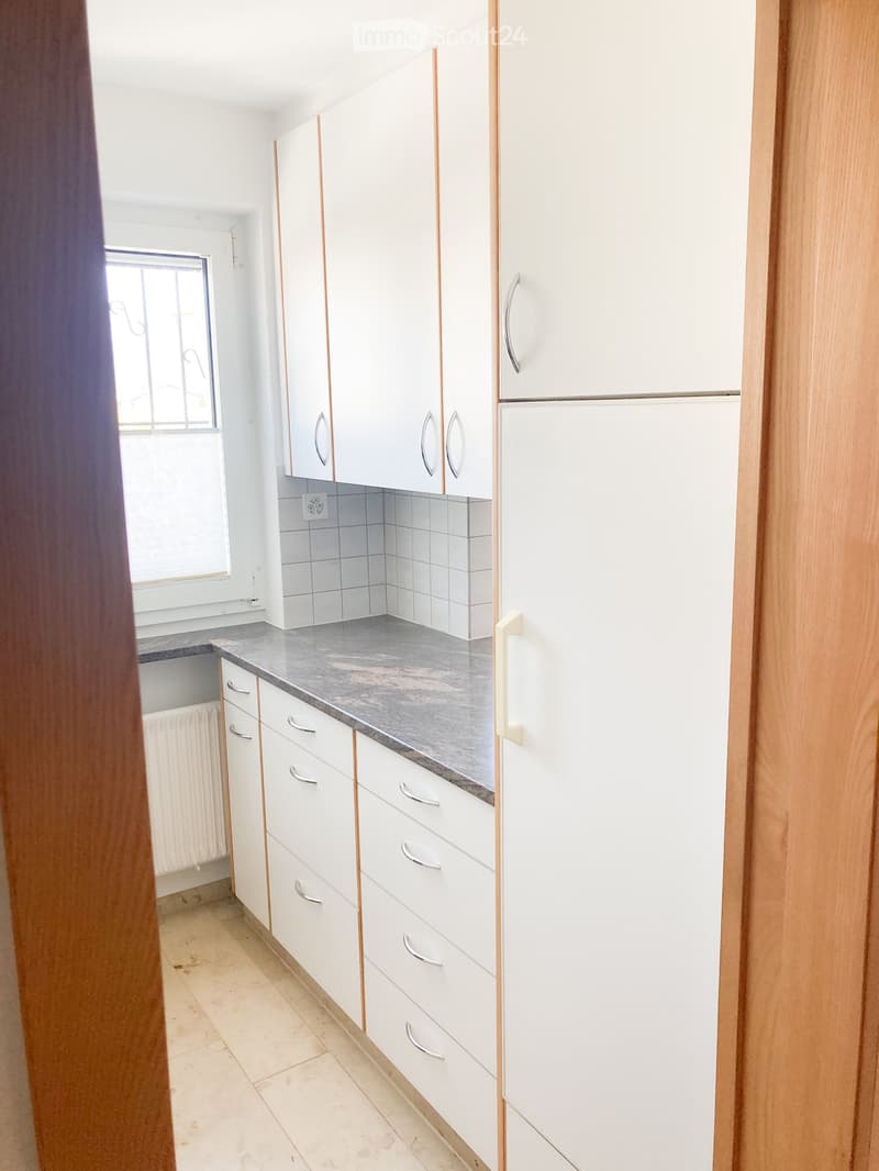 Modern kitchen with white cabinets, silver handles, and a grey countertop. The backsplash is tiled in grey, and the floor is tiled in beige.