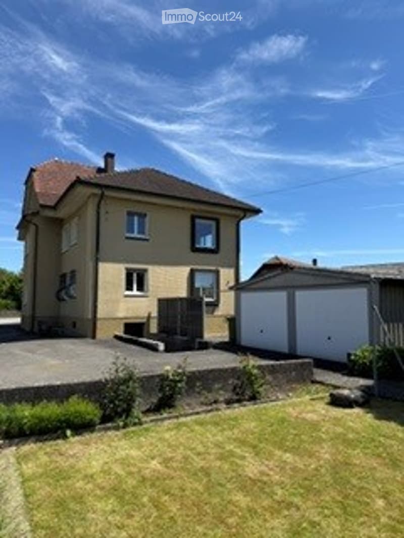 Two-story house with a red-tiled roof, white garage, and a small garden area.