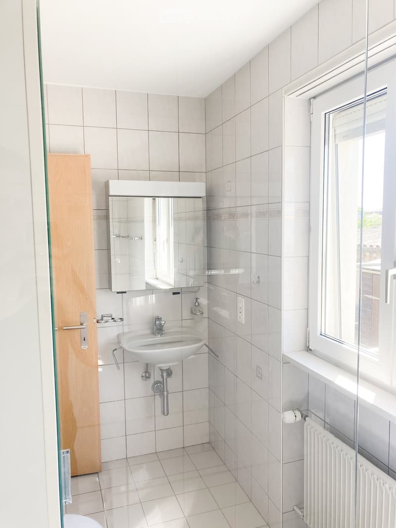 Modern bathroom with white tiles, a sink, a mirror, and a radiator near the window.