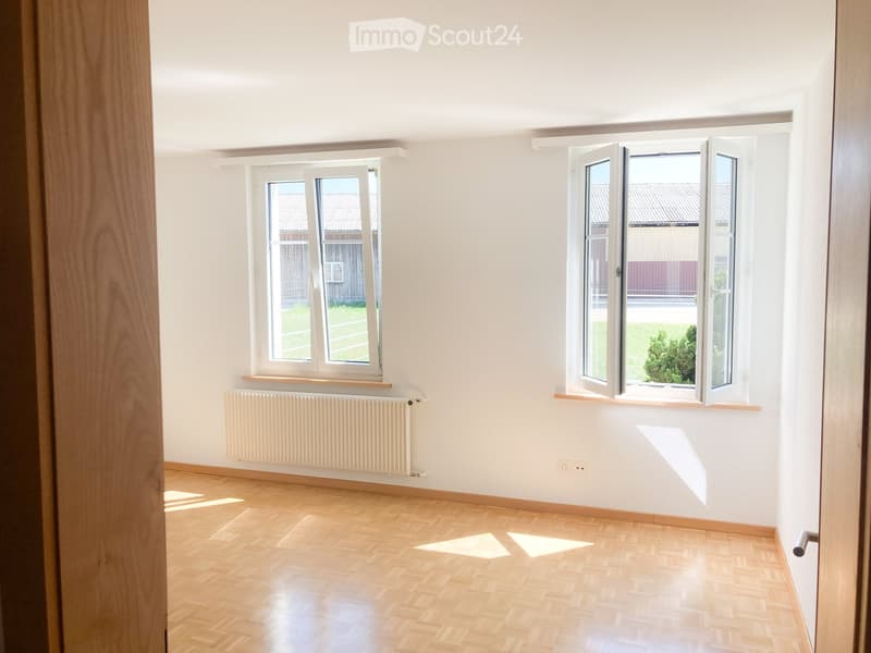 Empty room with light wooden flooring, white walls, and two windows with open shutters. A radiator is mounted on one wall.