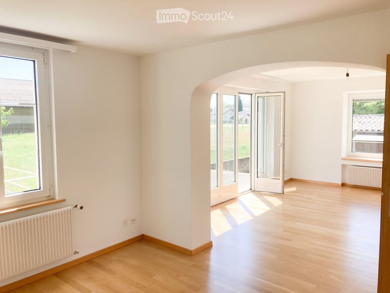 Empty room with light wooden flooring, white walls, large windows, and a sliding glass door leading to an outdoor area.