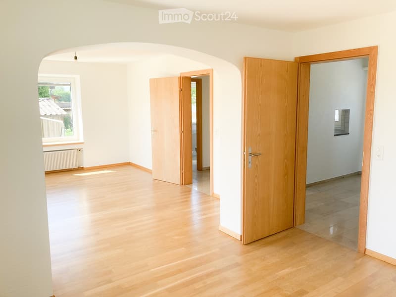 Empty room with light wooden flooring, white walls, and several open wooden doors leading to other spaces.
