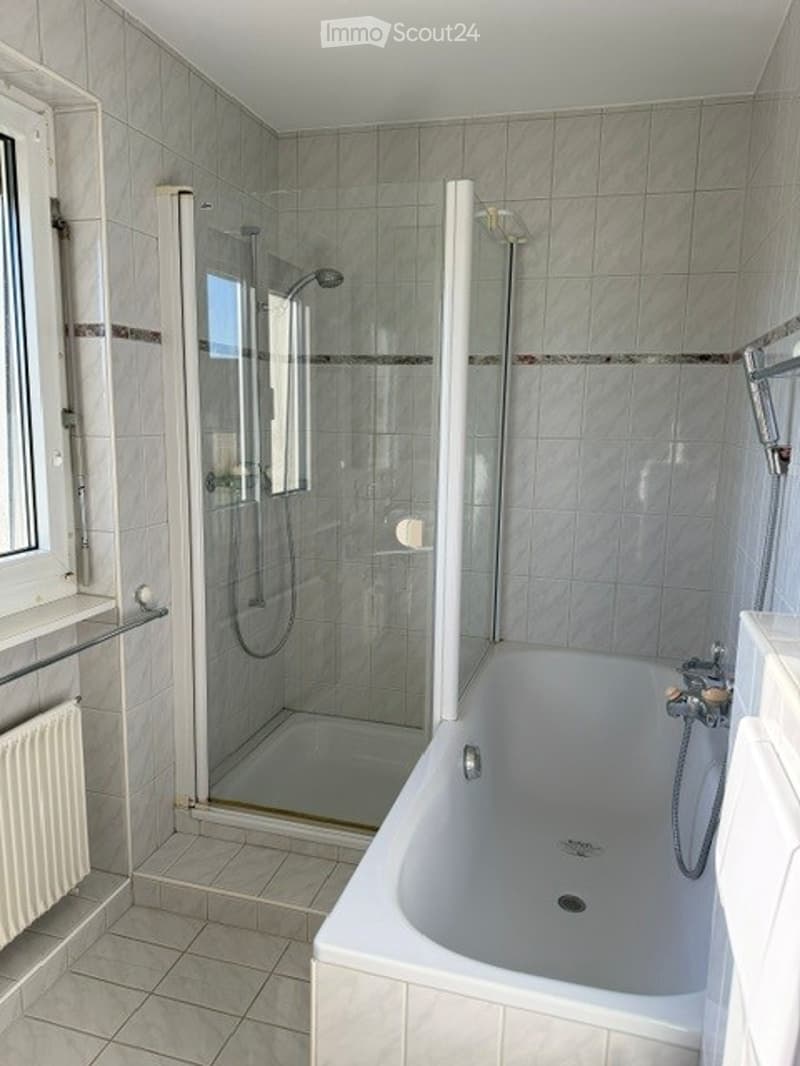 Modern bathroom with a bathtub, glass-enclosed shower, tiled walls, and a radiator.