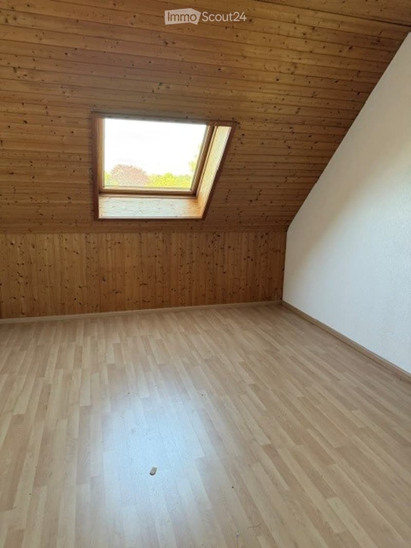 Empty attic room with wooden walls and floor, skylight window, no furniture or equipment.