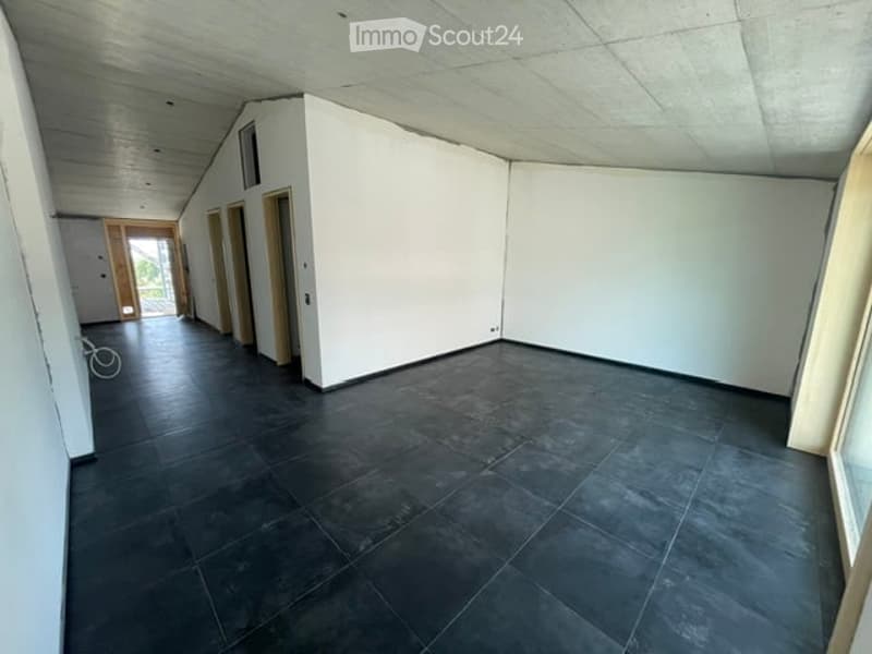 Empty room with white walls, dark tiled floor, and wooden doors leading to other spaces.