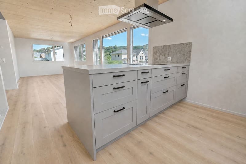 Modern kitchen with light grey cabinets, a central island, and large windows offering a scenic view.