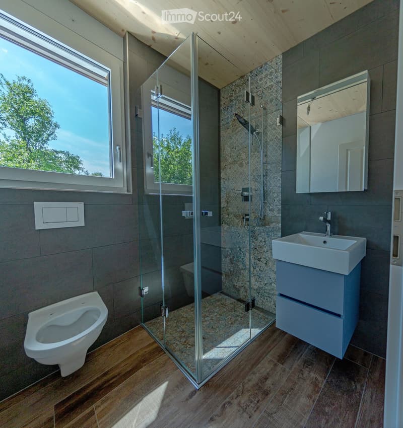 Tiled floor, modern glass shower enclosure, white ceramic sink, wooden walls, natural light from window