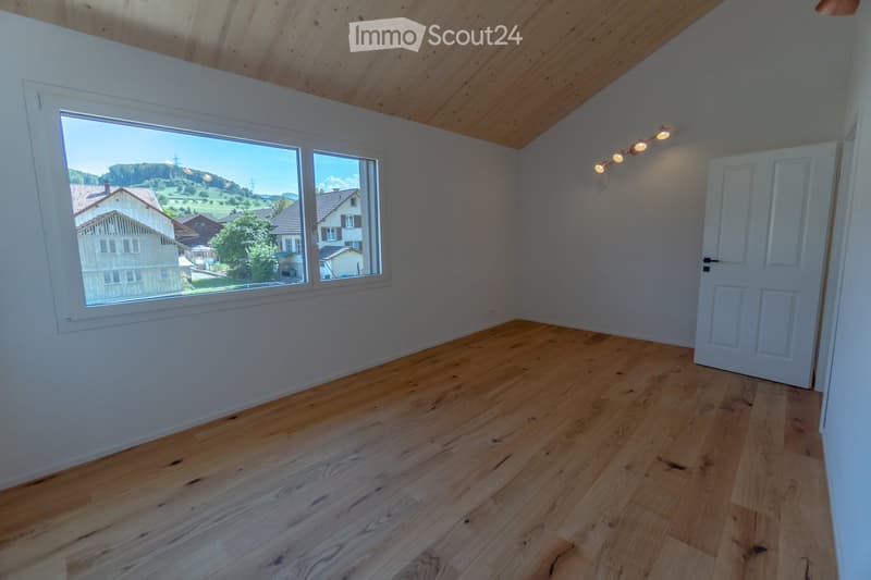 Empty room with wooden floor, white walls, large window, row of lights