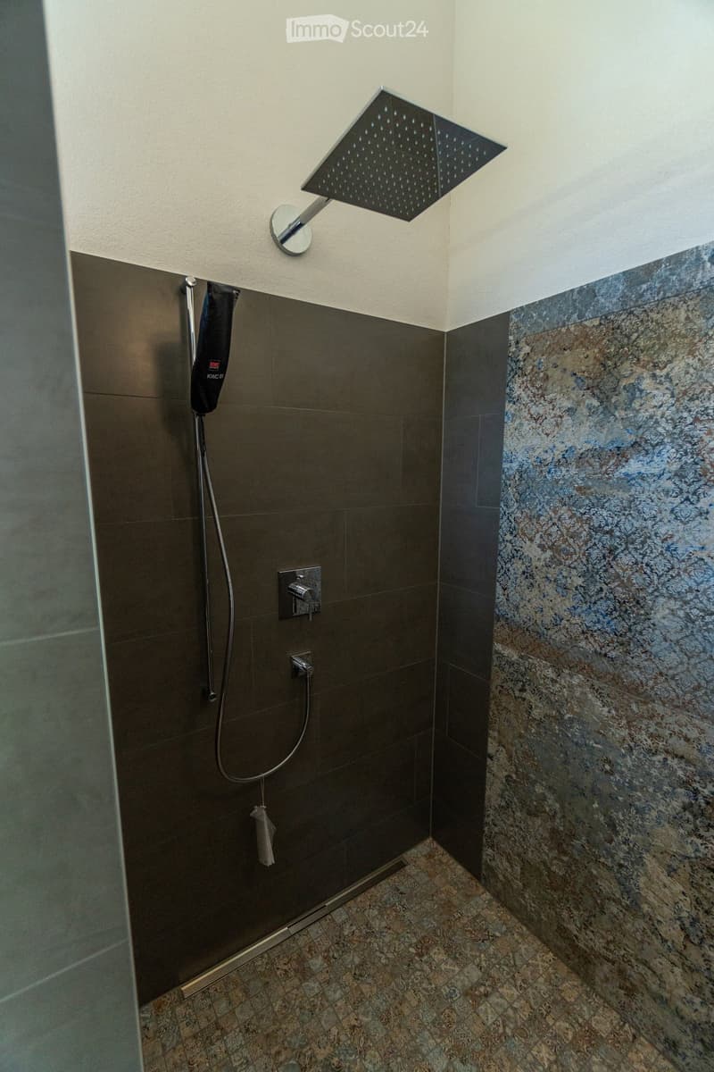 Square tiled shower with overhead showerhead and hanging handheld showerhead, curved tiles and wall decoration