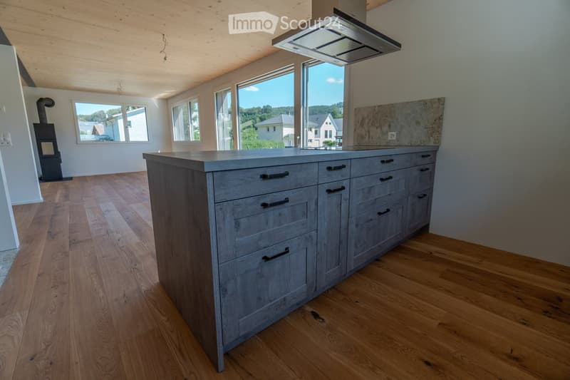 Empty kitchen with wooden floor, gray cabinets, large windows, granite countertop, gas stove.