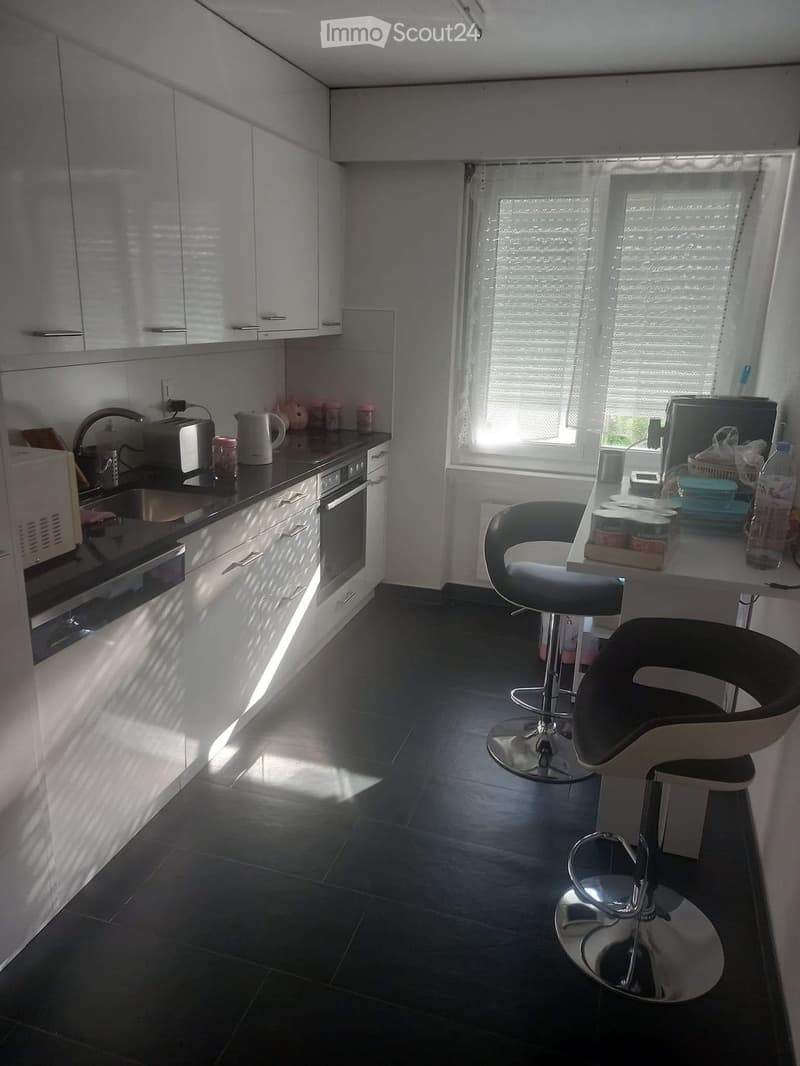 modern kitchen with white cabinets, black countertops, stainless steel appliances, and a window with blinds
