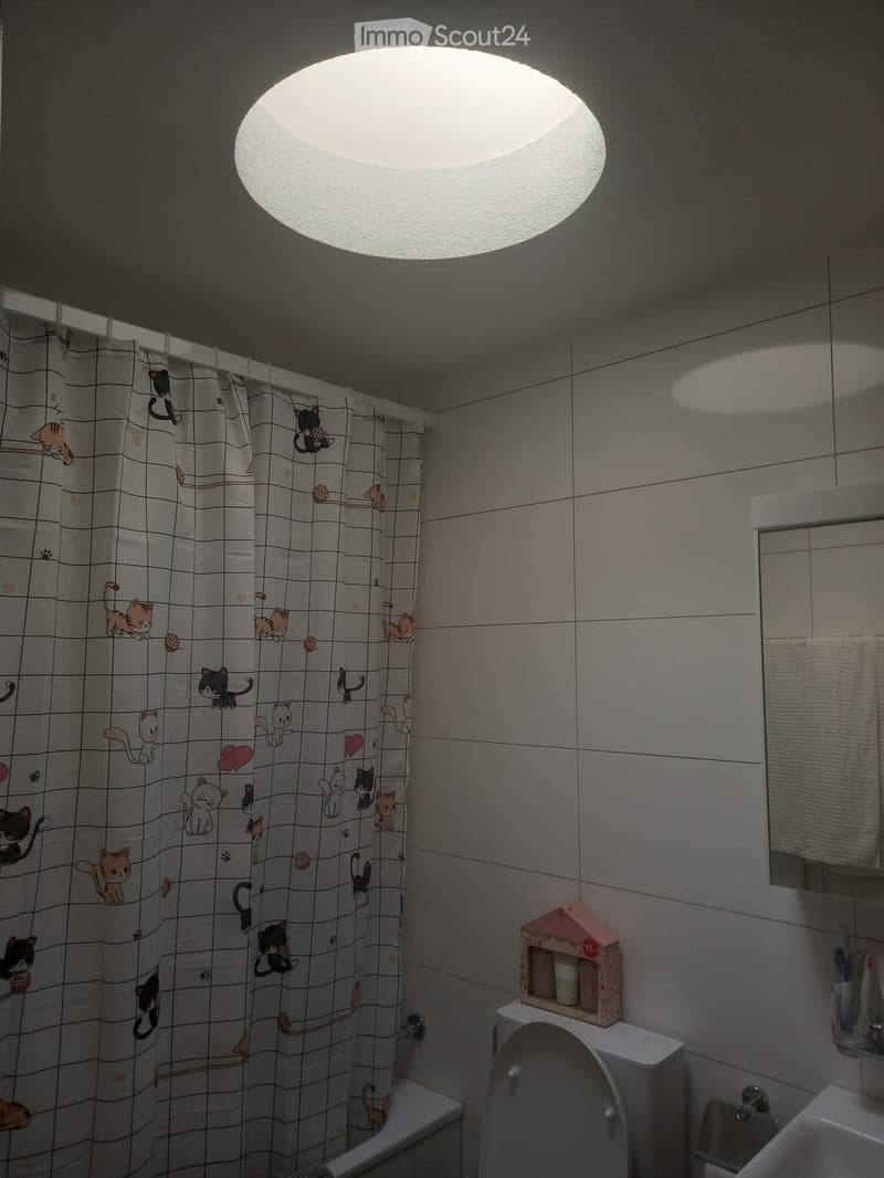 Bathroom with white tiles, a bathtub, a toilet, a sink, a mirror, and a cat-themed shower curtain.