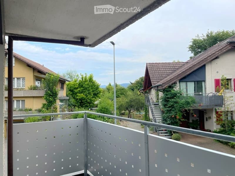 Balcony with grey metal railing, overlooking a residential area with houses, trees, and a staircase leading down.