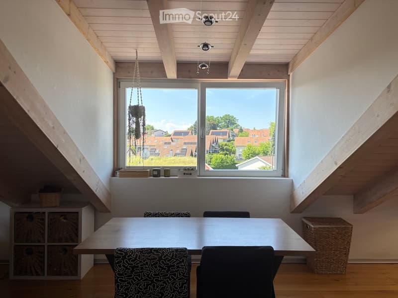 Bright, airy room with wooden ceiling beams, large windows overlooking a suburban neighborhood, a dining table with chairs, a storage unit, and decorative items on the windowsill.