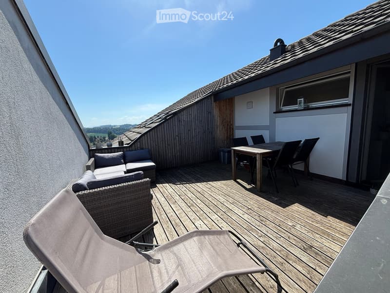 Wooden balcony with lounge sofa, dining table, chairs, and lounge chairs, overlooking a scenic landscape.