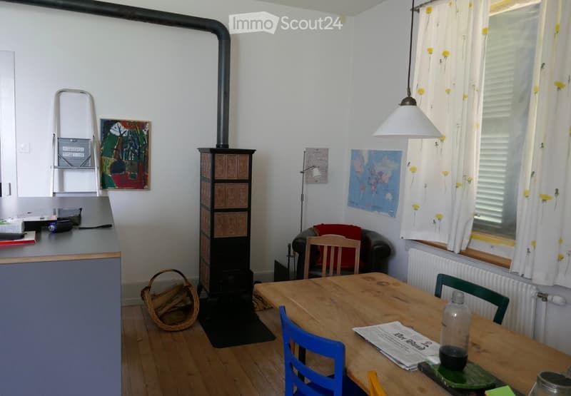 Cozy living and dining area with a wooden table, chairs, sofa, fireplace, and various decorations including a painting and a world map.