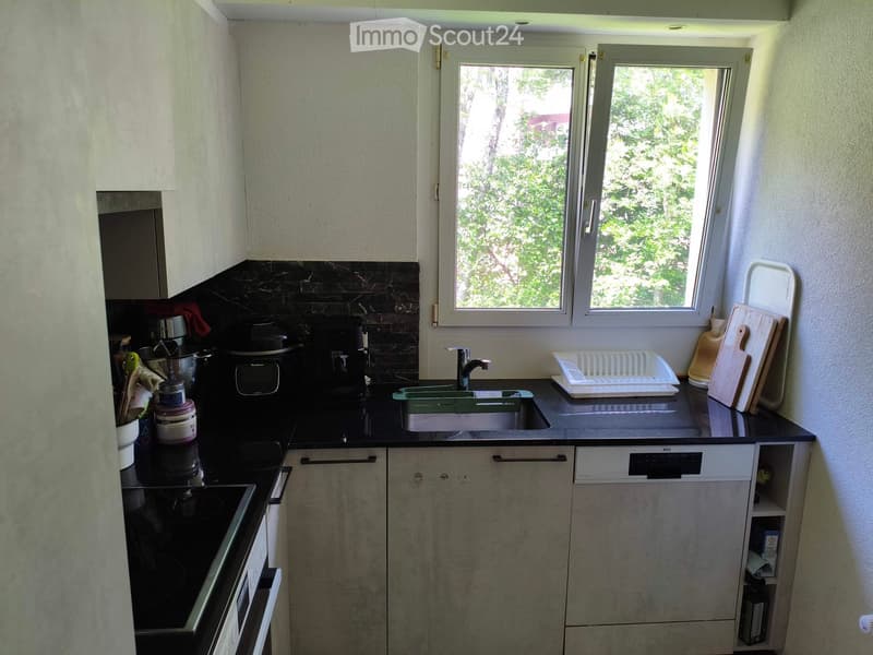 Modern kitchen with grey cabinets, black countertop, sink, faucet, dish rack, cutting board, oven, coffee maker, and microwave.