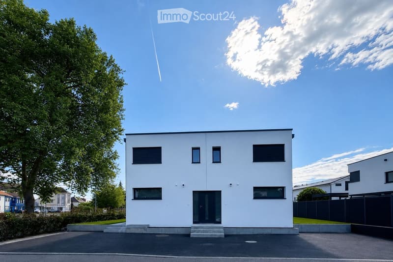 Modern single-story house with white exterior, large windows, and a raised ground floor entrance.