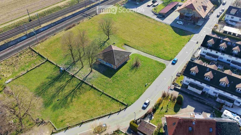 Aerial view of a residential area with multiple houses, a small park, and a railway line in the background.