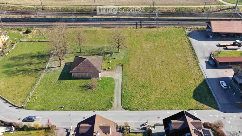 Aerial view of a large, open green field with a small building, surrounded by roads and nearby structures.