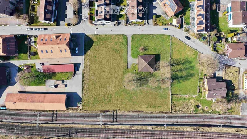 Aerial view of a residential area with multiple houses, roads, and a train track running through the lower portion of the image.