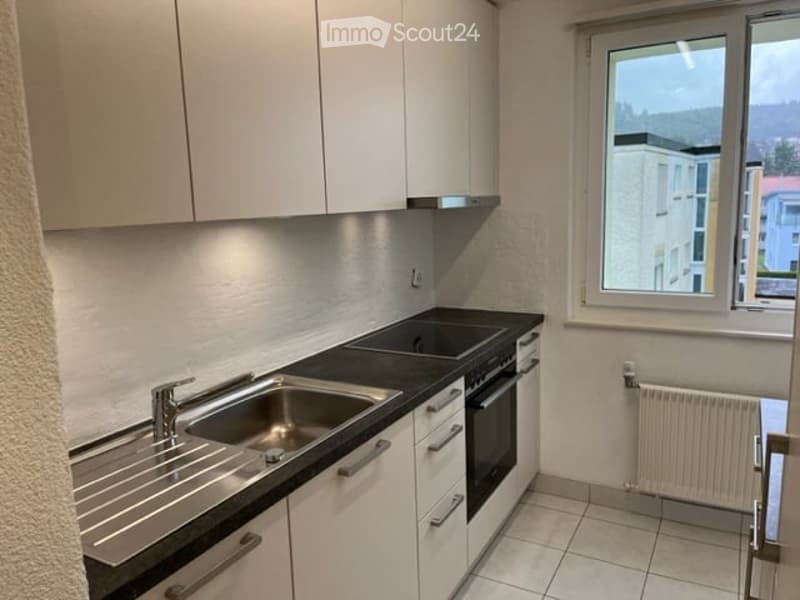 Modern kitchen with white cabinets, stainless steel sink, oven, and a window offering a view of the surrounding area.