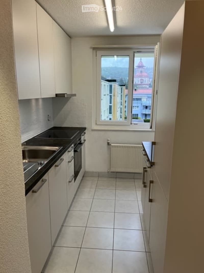 Modern kitchen with white cabinets, stainless steel sink, oven, and radiator. Large window offers a view of the city.