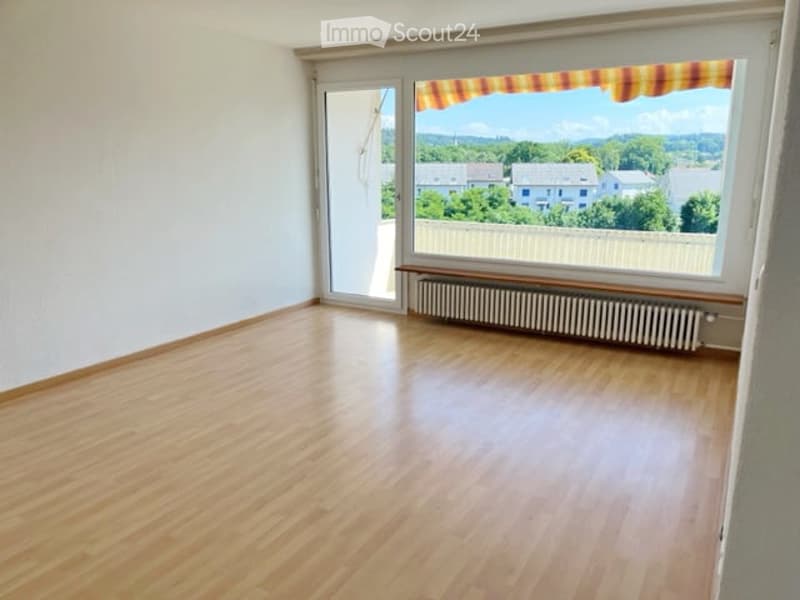 Empty room with wooden flooring, large window with view, radiator, and sliding glass door leading outside.