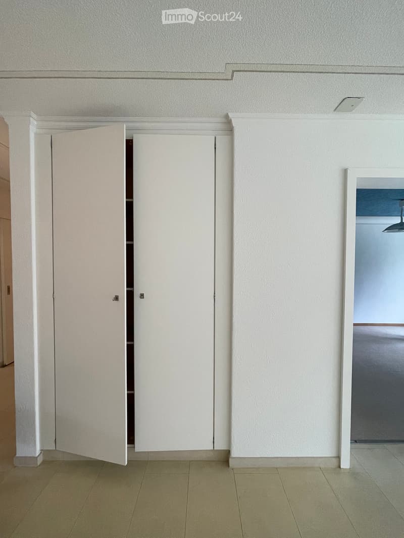 Empty room with white walls, tiled floor, and a set of white double doors leading to another space.