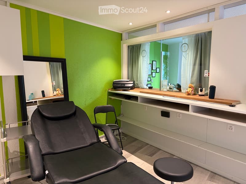 Modern room with green and white striped walls, a large black massage chair, a small stool, a white counter with a printer, a cup, and a flower arrangement.