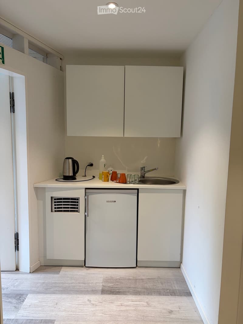 Compact kitchen with white cabinets, a small refrigerator, a sink, and various kitchen items on the counter.