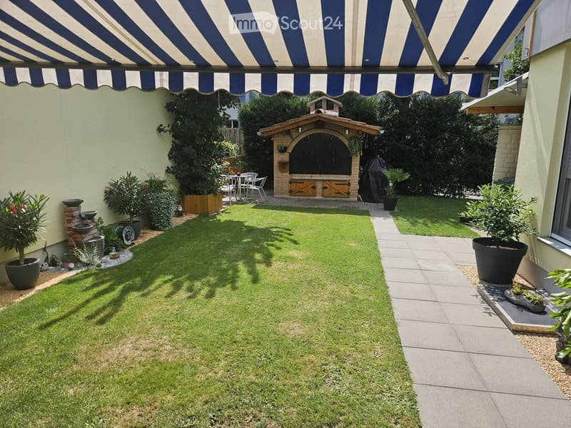 Well-maintained garden with a central lawn, surrounding potted plants, a small fountain, a covered outdoor seating area, and a brick barbecue structure.