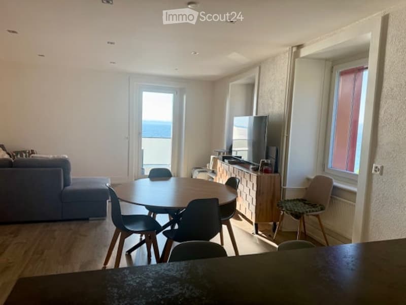 Modern furnished room with a round table, chairs, couch, entertainment center, and a television. It has a view of the ocean.