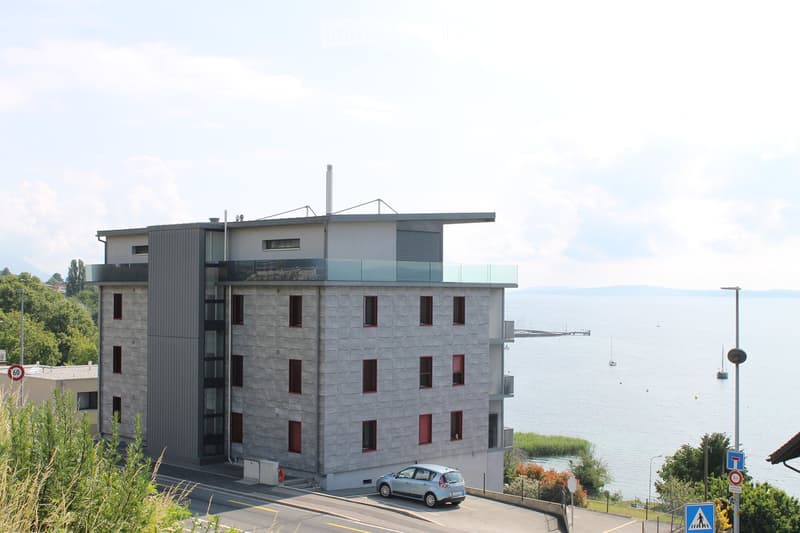 Modern apartment building with glass balconies, overlooking a lake and mountains
