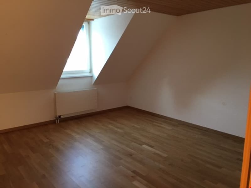 Empty attic room with wooden flooring, slanted ceiling, and a single window letting in natural light. No furniture or equipment present.