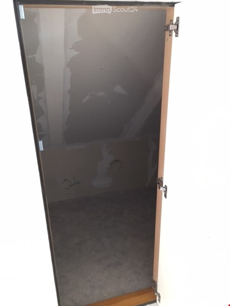 An empty room with a glass door leading to a concrete floor area. The walls are unfinished, showing exposed plaster and some debris on the floor.