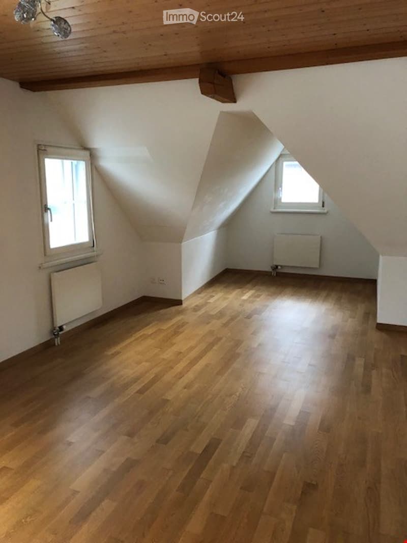 Empty attic room with wooden flooring, white walls, and two windows with slanted ceilings.