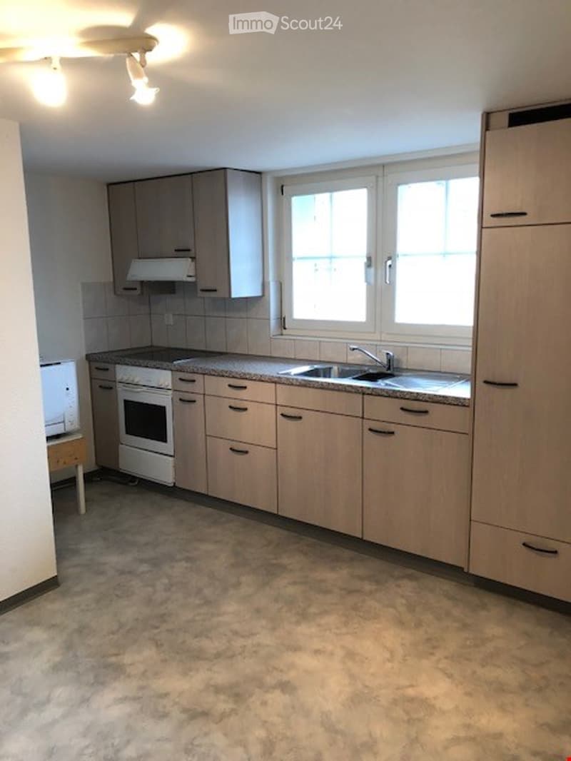 Modern kitchen with light wooden cabinets, a sink with a faucet, an oven, and a microwave. The countertop is visible, and the floor is tiled.