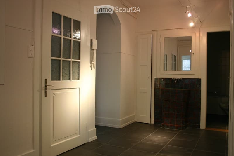 Hallway with dark tiled floor, white walls, arched doorway, and a small bathroom visible at the end.