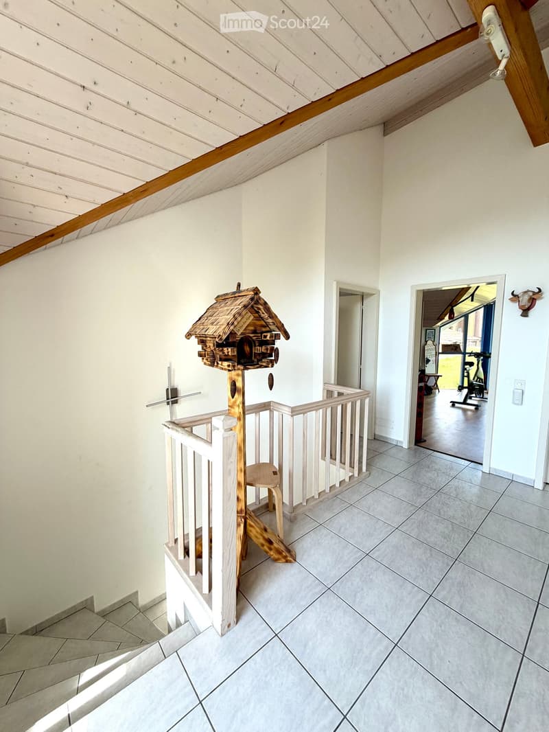 Staircase with wooden railing and a decorative birdhouse on the landing, leading to an open area with exercise bike and outdoor view.